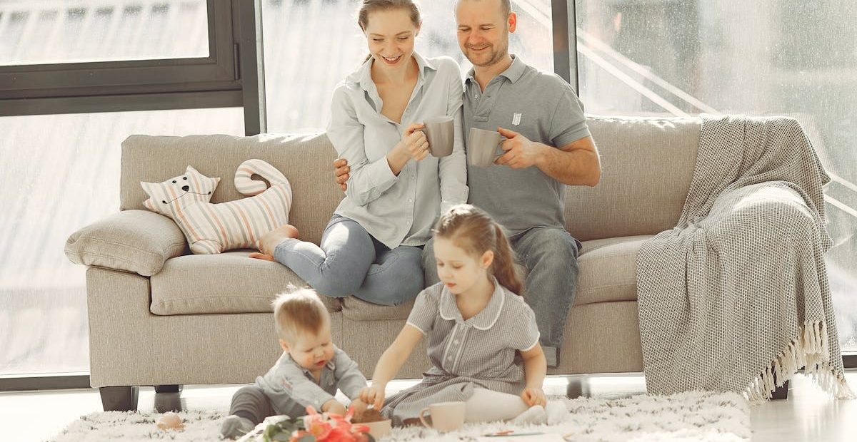 Cheerful family wearing casual clothes sitting in living room while playing and drinking tea during weekend at home in morning